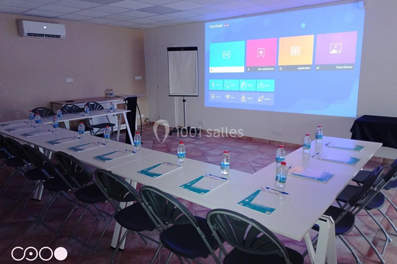 Salle Madrague Salle de réunion équipée avec tables en U, chaises, écran de projection, paperboard et documents disposés sur les tables.