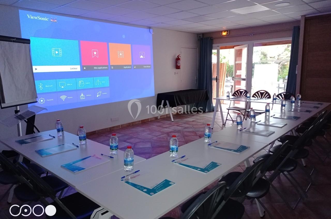 Salle Madrague Salle de réunion équipée d'un projecteur affichant un écran d'accueil, tables disposées en U avec documents et bouteilles d…