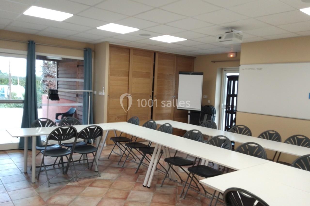Salle Madrague Salle de réunion lumineuse avec tables disposées en U, chaises noires, tableau blanc et paperboard.