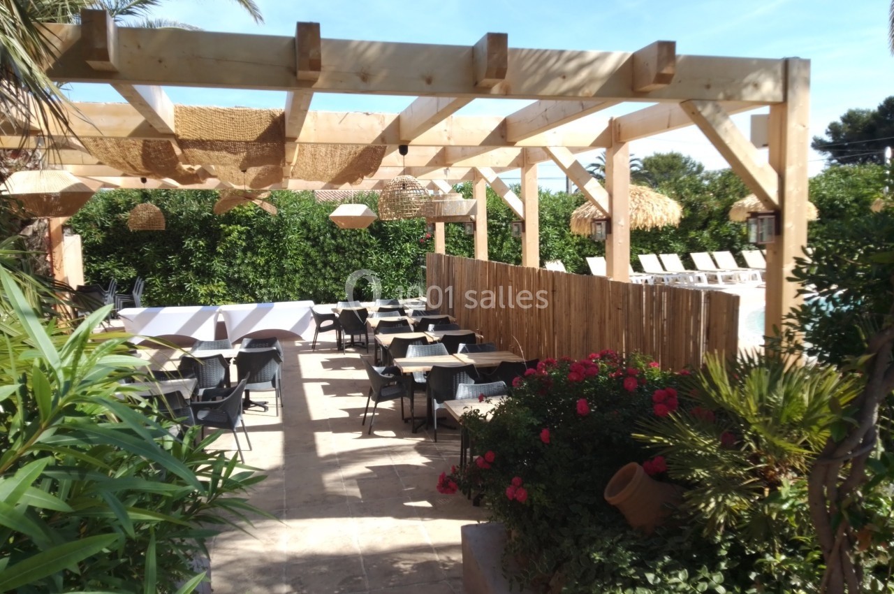 Terrasse restaurant La Réserve Terrasse extérieure avec pergola en bois, tables et chaises, entourée de végétation et fleurs colorées.