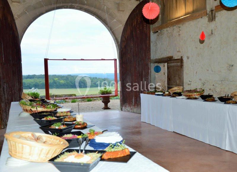 Buffet dressé dans une salle rustique avec vue sur un paysage champêtre à travers une grande ouverture voûtée.