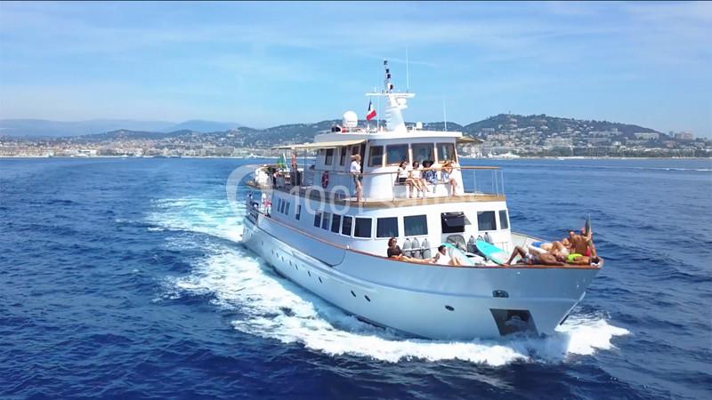 Un yacht blanc navigue sur une mer calme par temps ensoleillé, avec des passagers profitant du pont.