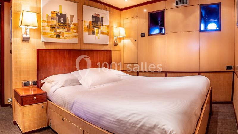 Lit double avec draps blancs dans une chambre lumineuse aux murs en bois clair, décorée de tableaux modernes.