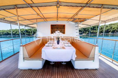 Un bateau à moteur tracte une bouée gonflable sur une mer calme, avec un yacht et une côte boisée en arrière-plan.