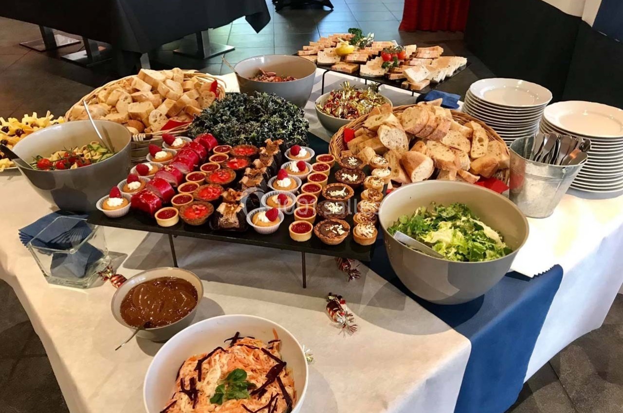 Buffet varié avec plats froids, salades, pains, sauces et desserts disposés sur une table blanche.