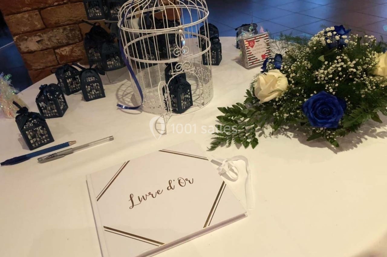 Livre d'or posé sur une table décorée avec une cage blanche, des petites lanternes et un bouquet de fleurs.