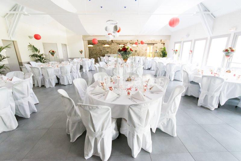 Salle de réception décorée avec des tables rondes, nappes blanches, centres de table fleuris et lanternes rouges suspendues.