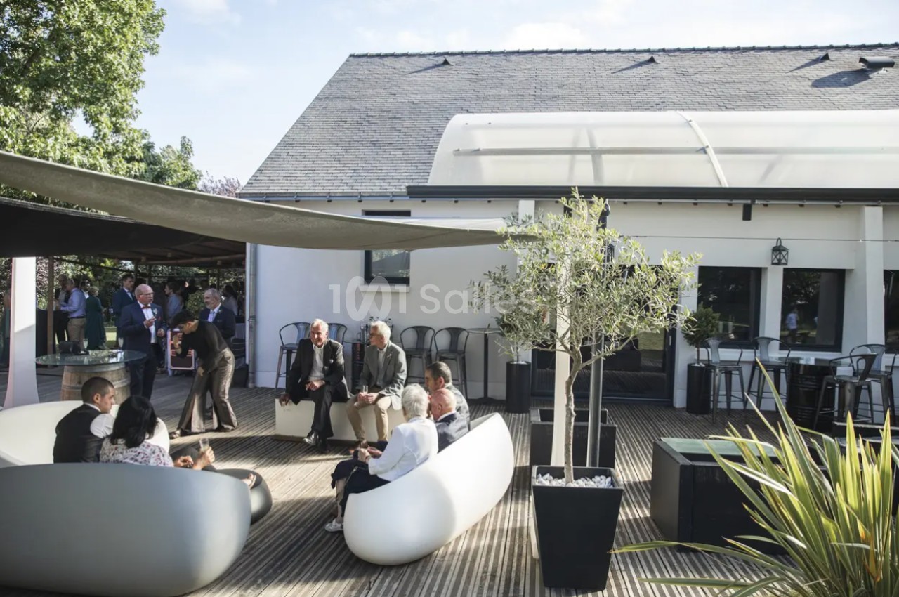 Personnes assises et discutant sur une terrasse en bois aménagée avec des fauteuils modernes et des plantes.