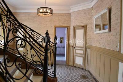 Vue d'un couloir lumineux menant à une chambre avec un lit, des murs clairs et un tapis au sol.