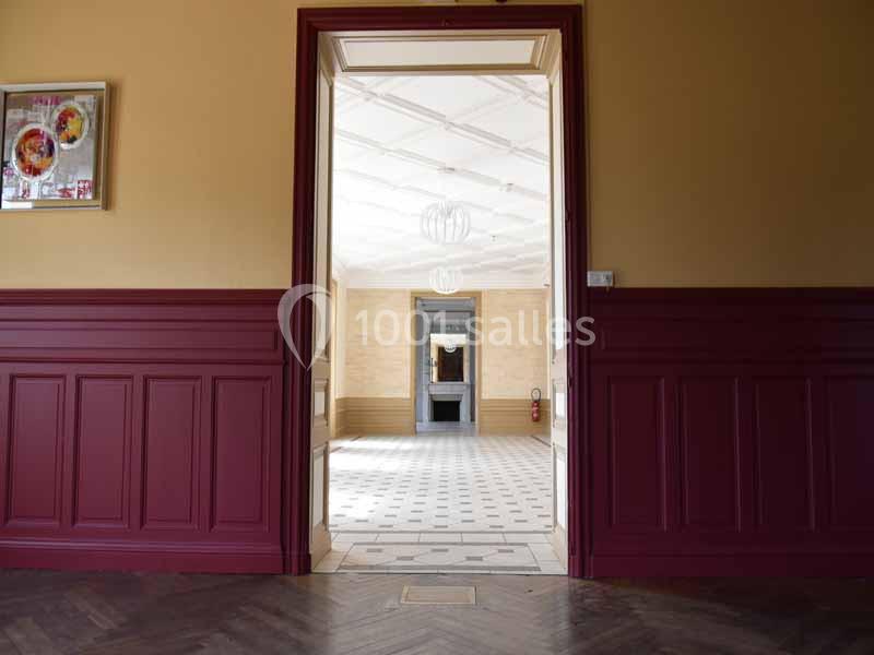 Vue d'une pièce lumineuse avec un sol carrelé, encadrée par une porte en bois rouge et des murs beige et rouge.