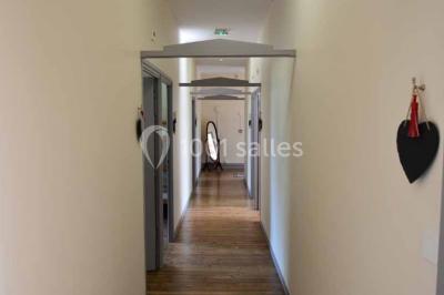 Vue d'un couloir lumineux menant à une chambre avec un lit, des murs clairs et un tapis au sol.