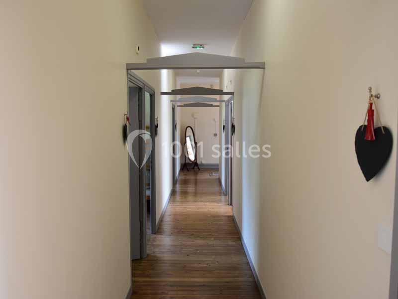 Couloir lumineux avec parquet en bois, portes sur les côtés et un miroir au fond près d'un mur clair.