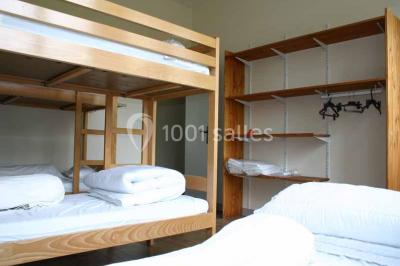 Vue d'un couloir lumineux menant à une chambre avec un lit, des murs clairs et un tapis au sol.