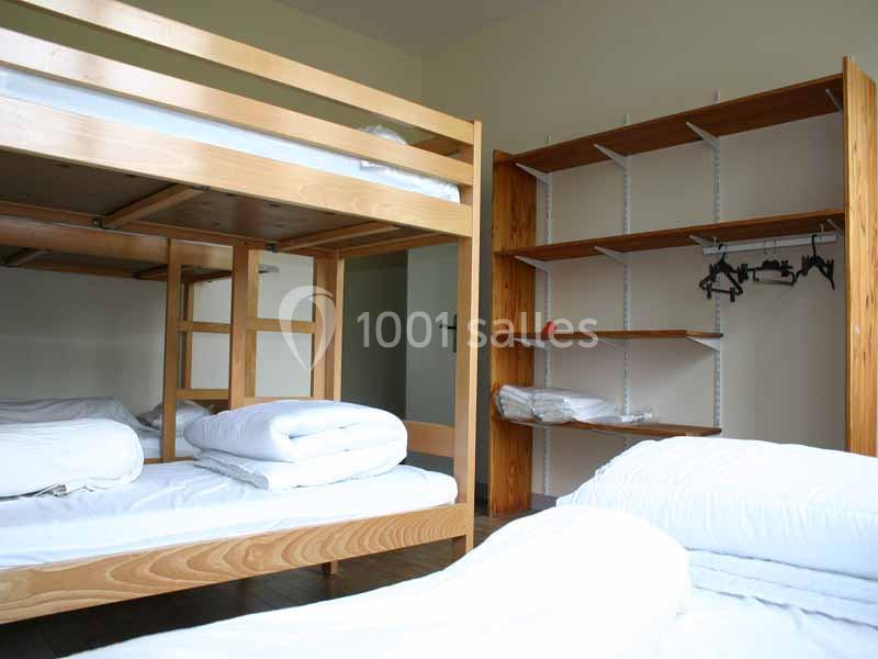 Chambre avec lits superposés en bois, étagères ouvertes et literie blanche pliée sur les lits.