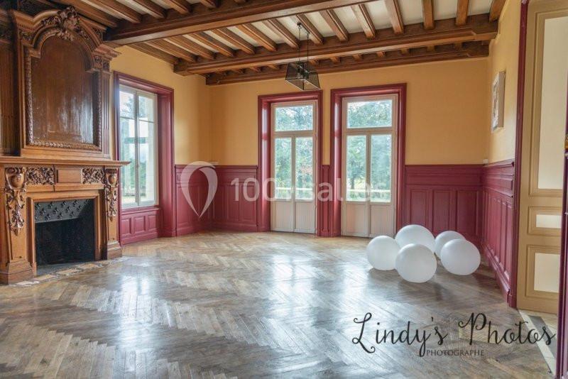 Salle lumineuse avec parquet en bois, cheminée sculptée, murs colorés et trois ballons blancs posés au sol.