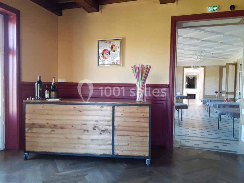 Un meuble en bois avec des bouteilles et des pailles colorées, situé près d'une entrée menant à une salle lumineuse.