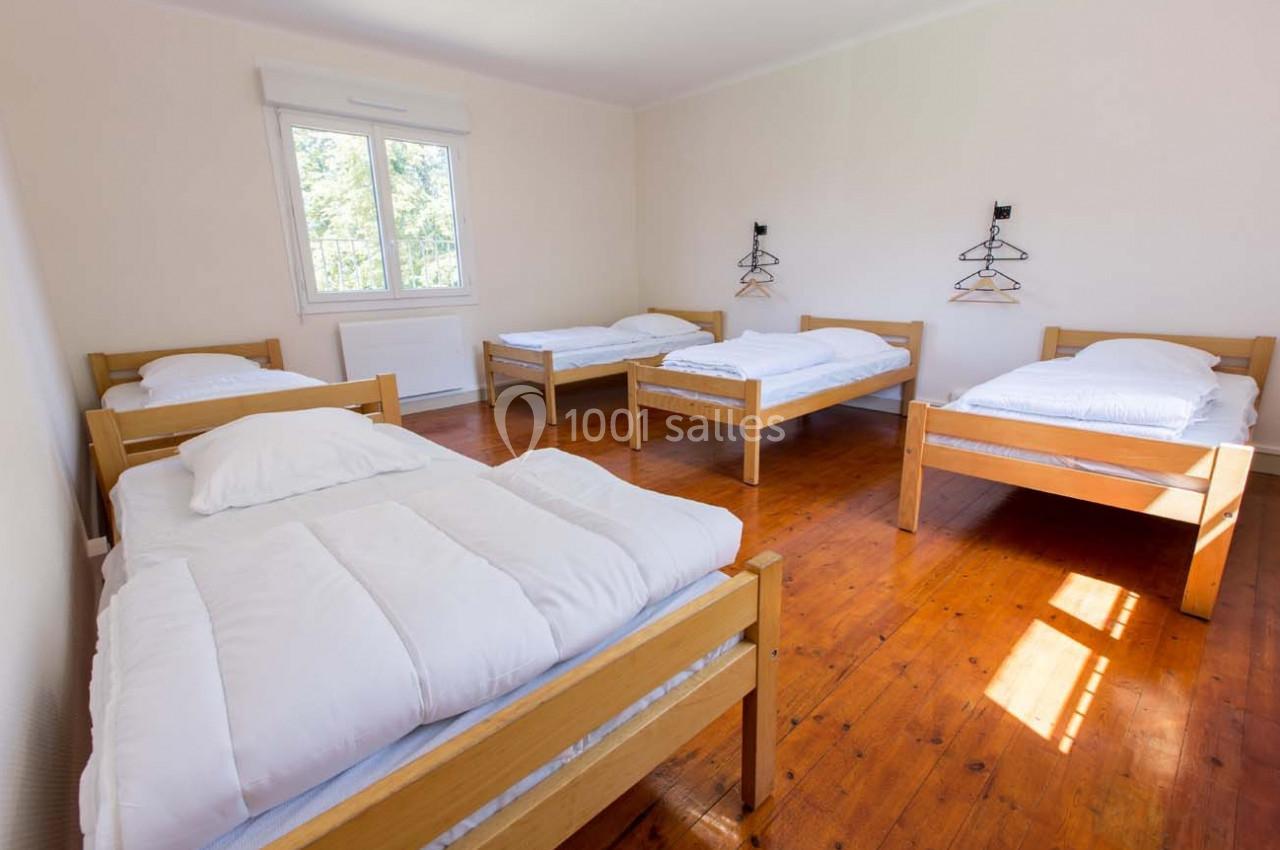 Chambre lumineuse avec cinq lits simples en bois, parquet au sol et fenêtre donnant sur l'extérieur.