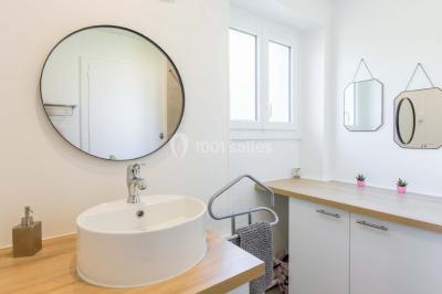 Vue d'un couloir lumineux menant à une chambre avec un lit, des murs clairs et un tapis au sol.