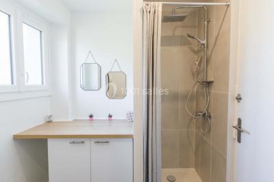 Vue d'un couloir lumineux menant à une chambre avec un lit, des murs clairs et un tapis au sol.