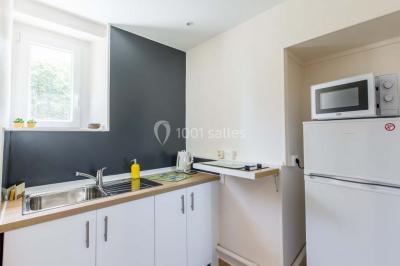 Vue d'un couloir lumineux menant à une chambre avec un lit, des murs clairs et un tapis au sol.