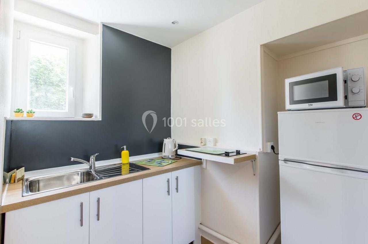 Cuisine compacte avec évier, plaques de cuisson, micro-ondes, réfrigérateur et fenêtre laissant entrer la lumière naturelle.