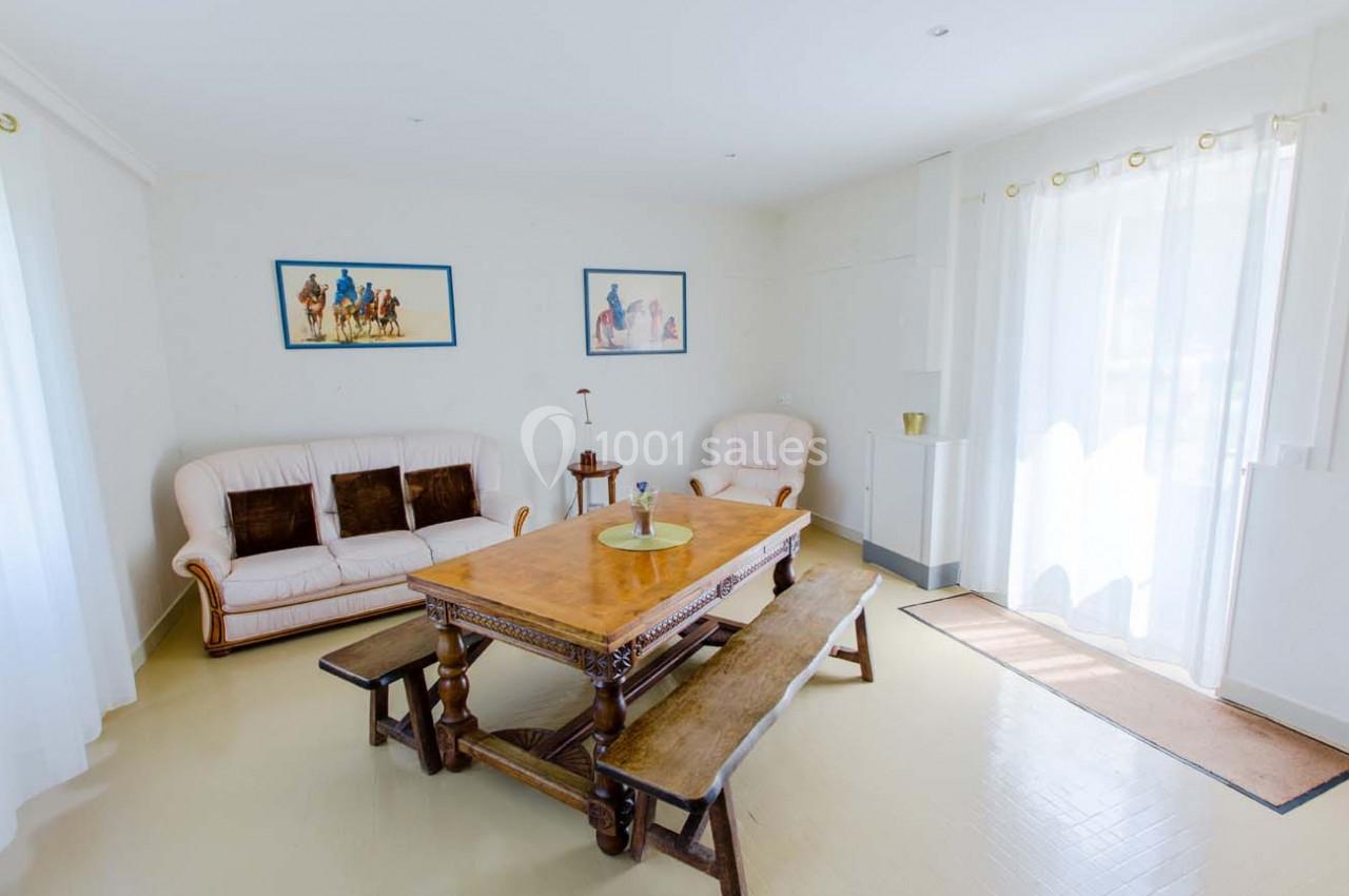 Salle de séjour lumineuse avec table en bois, bancs assortis, canapé beige et décorations murales.