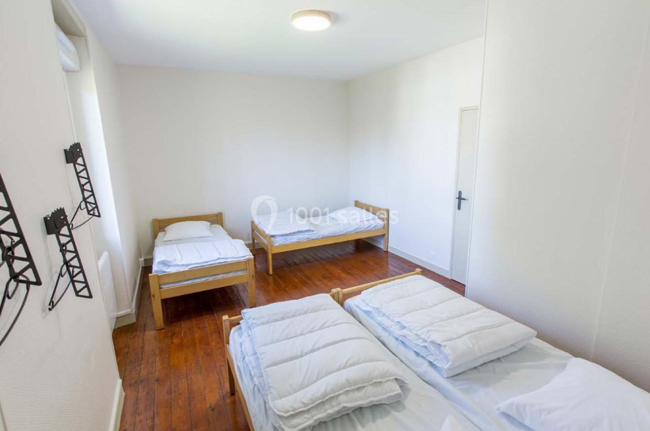 Chambre lumineuse avec quatre lits simples, parquet en bois et murs blancs, équipée de porte-manteaux muraux.