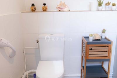 Vue d'un couloir lumineux menant à une chambre avec un lit, des murs clairs et un tapis au sol.