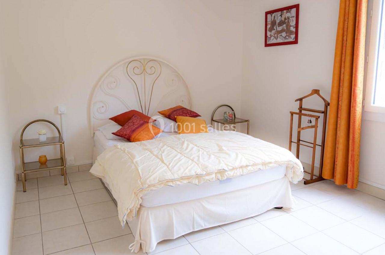 Chambre lumineuse avec un lit double, tête de lit en métal, coussins colorés, tables de chevet et rideaux orange.