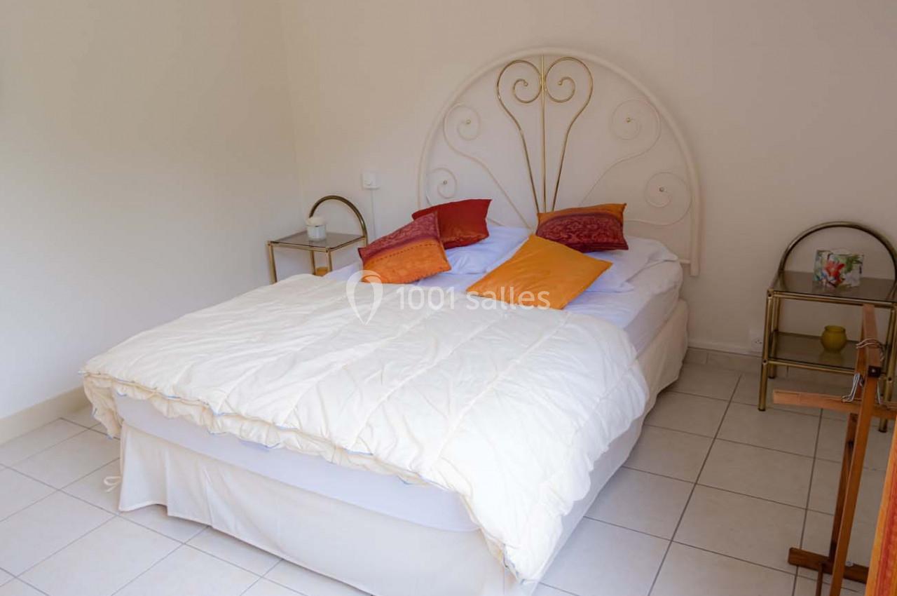 Lit double avec une tête de lit en métal blanc, draps clairs et coussins colorés, entouré de tables de chevet.