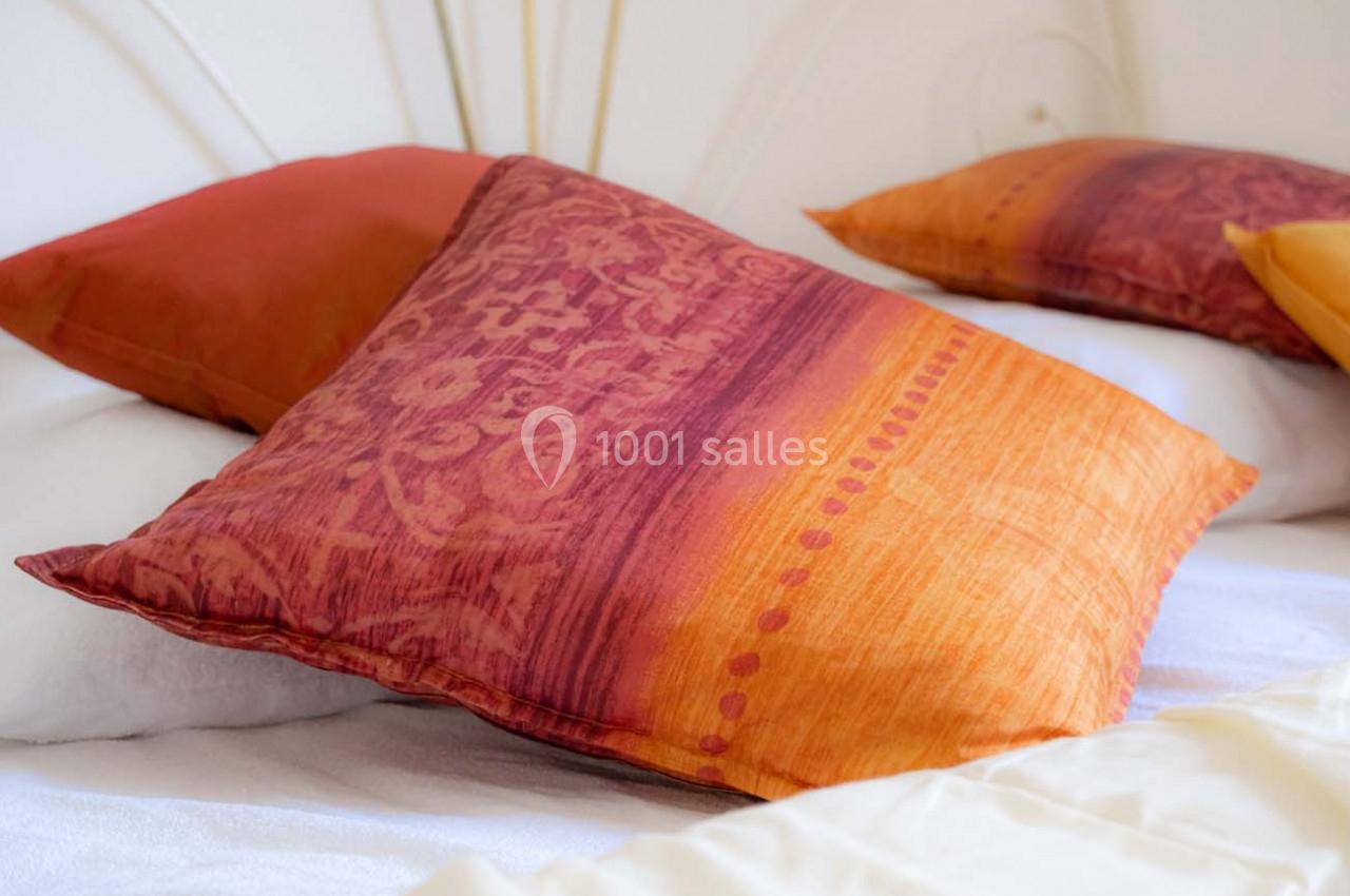 Deux oreillers aux motifs orange et rouge posés sur un lit avec des draps blancs.