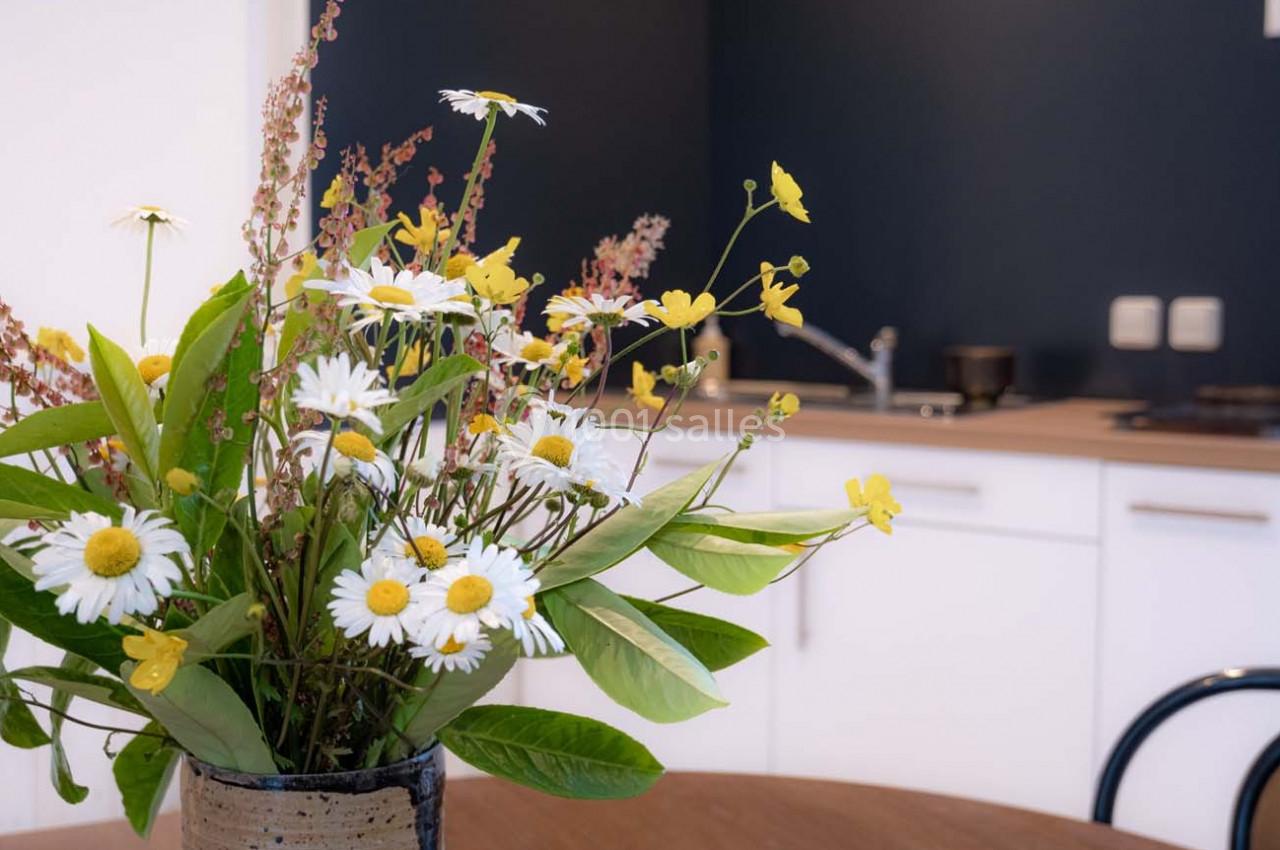Bouquet de fleurs sauvages dans un vase sur une table en bois, avec une cuisine moderne en arrière-plan.