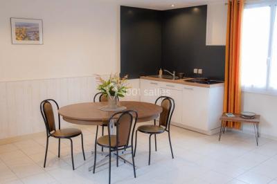 Vue d'un couloir lumineux menant à une chambre avec un lit, des murs clairs et un tapis au sol.