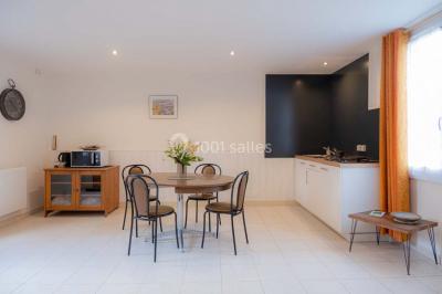 Vue d'un couloir lumineux menant à une chambre avec un lit, des murs clairs et un tapis au sol.