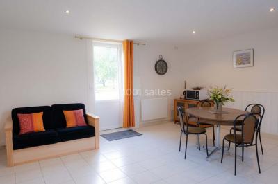 Vue d'un couloir lumineux menant à une chambre avec un lit, des murs clairs et un tapis au sol.