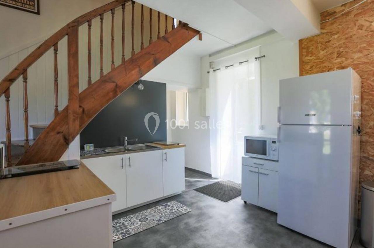 Cuisine moderne avec escalier en bois, équipée d'un réfrigérateur, d'un micro-ondes et de meubles blancs.