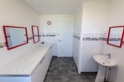 Vue d'un couloir lumineux menant à une chambre avec un lit, des murs clairs et un tapis au sol.