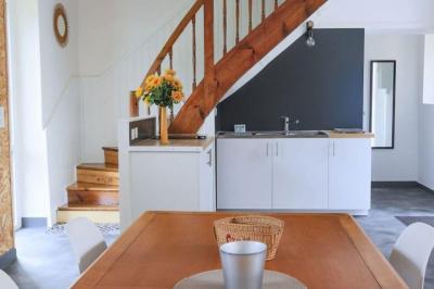 Vue d'un couloir lumineux menant à une chambre avec un lit, des murs clairs et un tapis au sol.