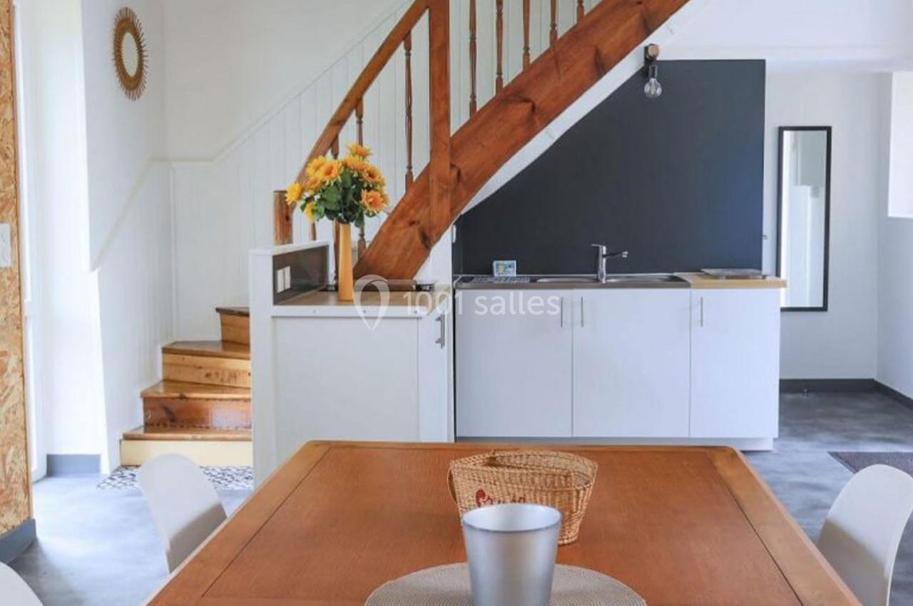 Cuisine ouverte avec escalier en bois, table en bois, bouquet de fleurs jaunes et mur noir en arrière-plan.