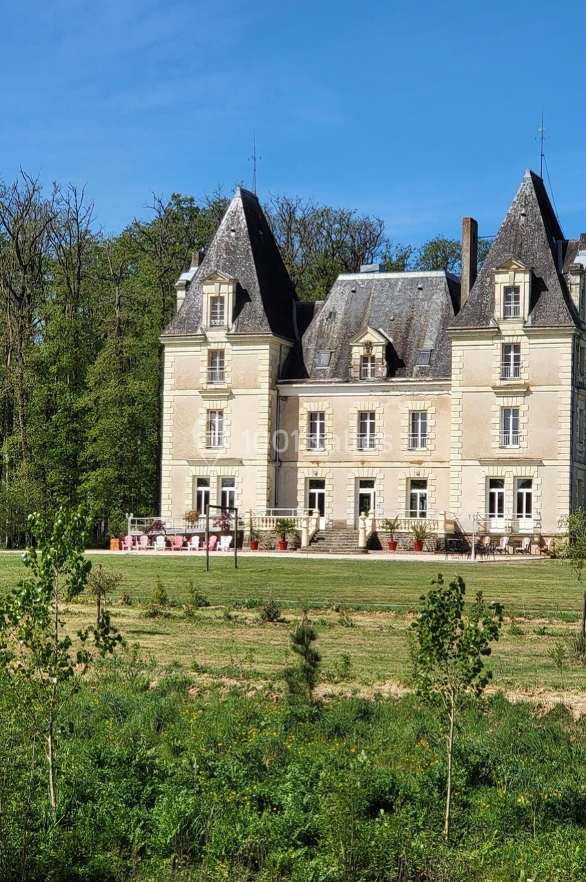 Location salle Chaumes-en-Retz (Loire-Atlantique) - Château de Noirbreuil #26 Château en pierre claire entouré de verdure, avec une terrasse aménagée et une forêt en arrière-plan.