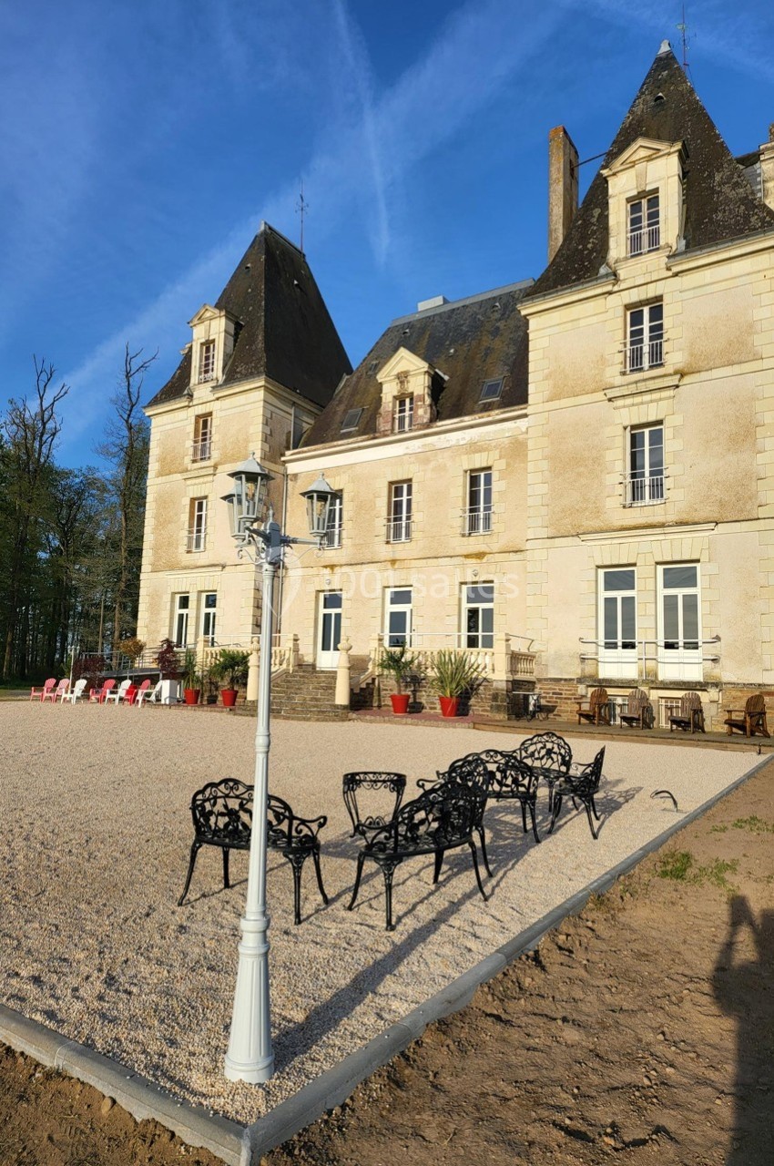 Location salle Chaumes-en-Retz (Loire-Atlantique) - Château de Noirbreuil #27 Façade d'un château en pierre avec des toits en ardoise, terrasse aménagée et mobilier extérieur sur une cour gravillonnée.