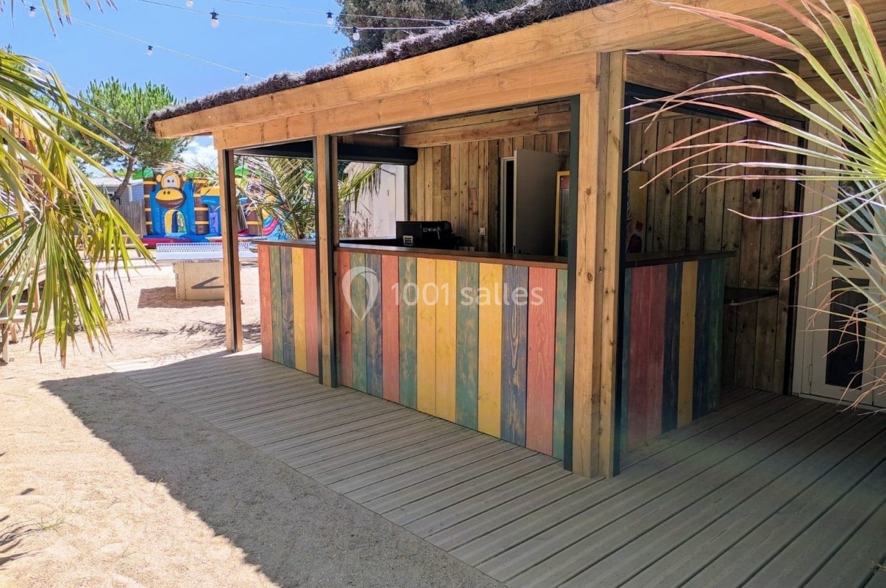 Kiosque en bois avec comptoir coloré, situé dans un espace extérieur entouré de palmiers et de décorations estivales.