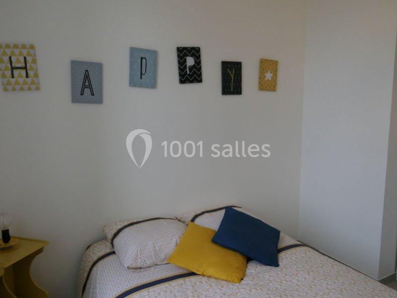 Lit avec coussins colorés dans une chambre lumineuse, décorée de cadres muraux formant le mot ’HAPPY’.