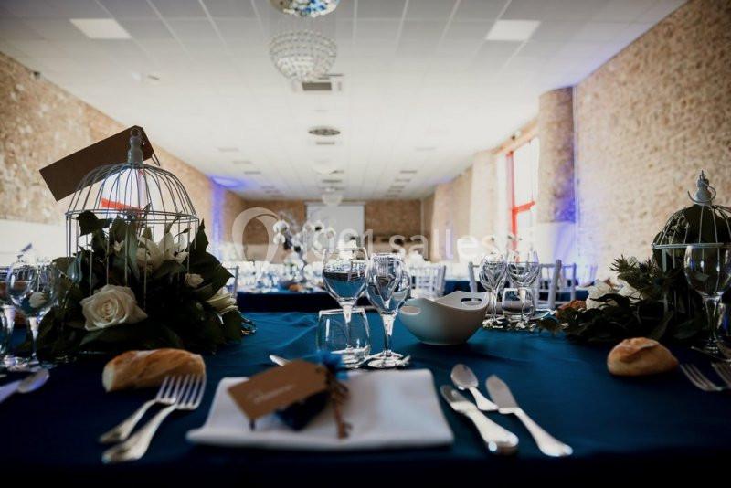 Table dressée pour un événement, avec nappes bleues, décorations florales, cages décoratives et couverts disposés.