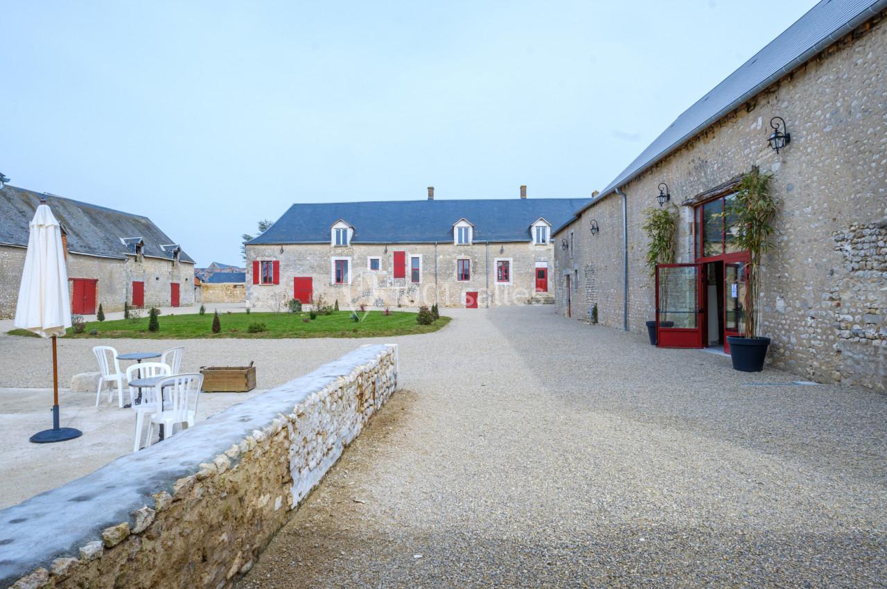 Cour d'une bâtisse en pierre avec des volets rouges, entourée de bâtiments annexes et de mobilier d'extérieur.