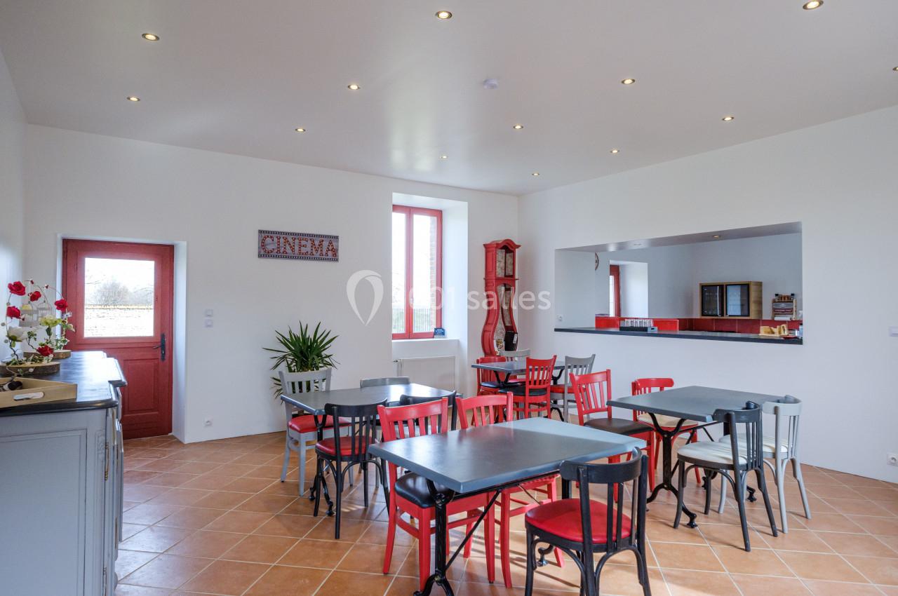 Salle lumineuse avec tables et chaises colorées, décorée d'une enseigne ’cinema’ et d'un comptoir rouge.