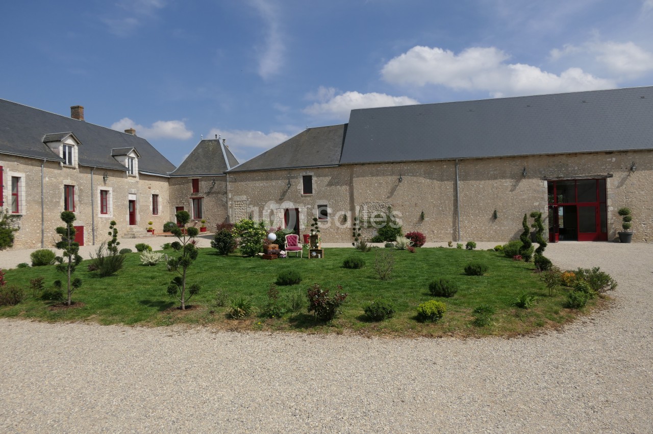 Cour intérieure d'un bâtiment en pierre avec pelouse centrale aménagée, entourée de buissons et d'arbres taillés.