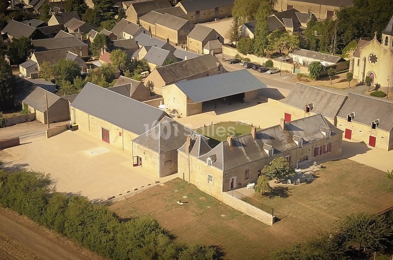Vue aérienne d'un ensemble de bâtiments en pierre avec cours centrale, entouré de végétation et d'autres habitations.