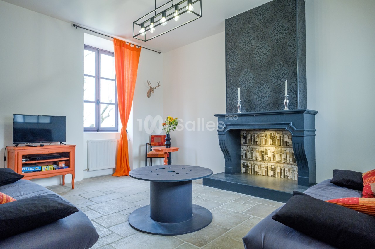 Salon lumineux avec cheminée décorative noire, table basse ronde, canapé, télévision et rideaux orange.