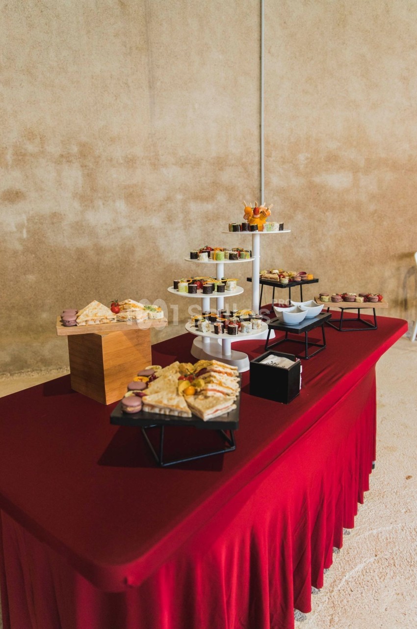 Buffet avec divers plats et desserts disposés sur une nappe rouge dans un espace intérieur sobre.